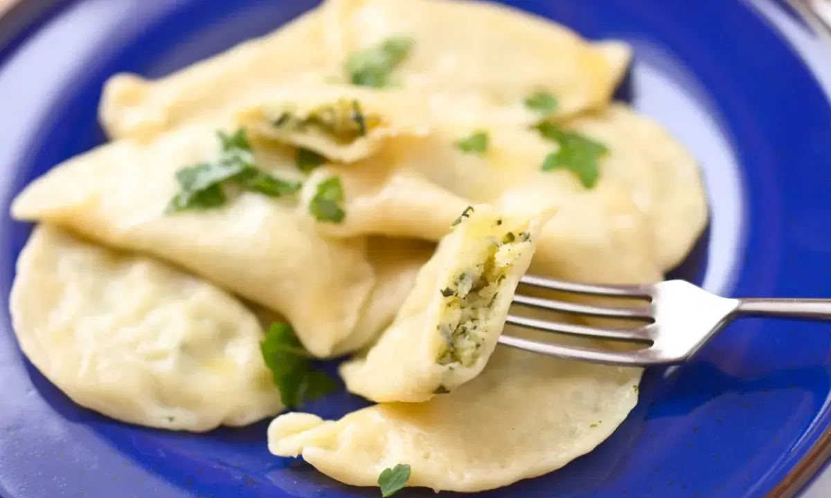 Pyszne pierogi ze szpinakiem, polane masłem i posypane natką pietruszki, czekają na widelcu.