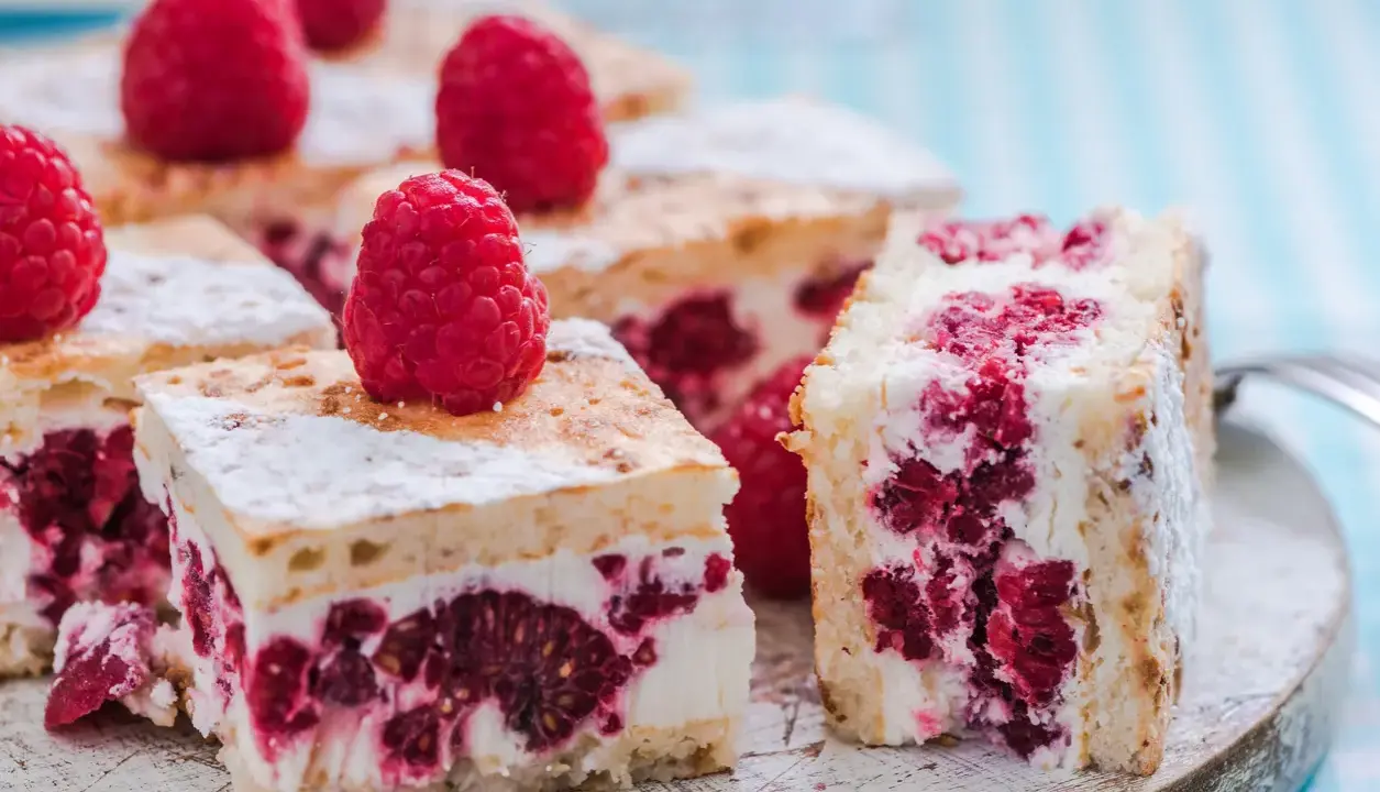 Pyszne ciasto z malinami i mascarpone, posypane cukrem pudrem, kusi soczystymi owocami i kremową konsystencją.