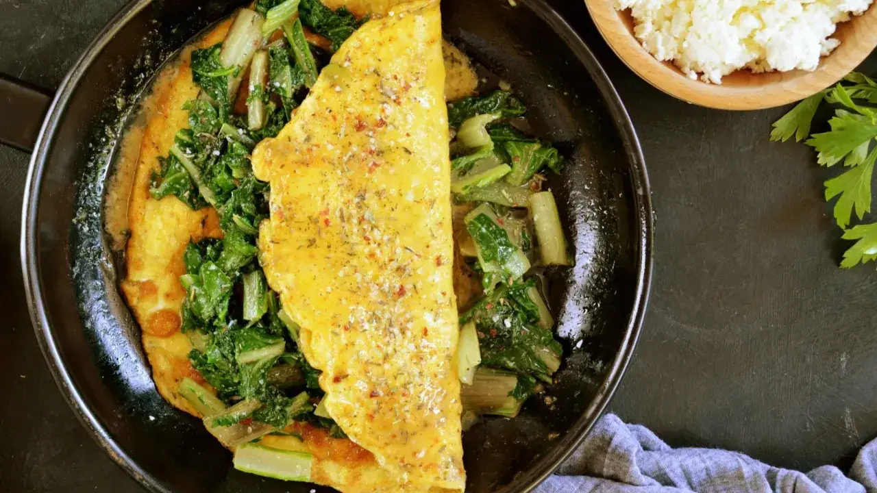 Pyszny omlet na słono z zielonymi warzywami, doprawiony ziołami. Obok miseczka białego sera i natka pietruszki.
