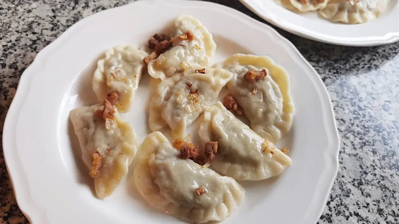 Pyszne pierogi z kapustą i grzybami, posypane skwarkami, na białym talerzu.