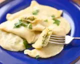 Pyszne pierogi ze szpinakiem, polane masłem i posypane natką pietruszki, czekają na widelcu.