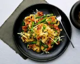 Pyszny makaron ze szparagami, chrupiącym boczkiem i parmezanem na czarnym talerzu. Idealny na wiosenny obiad.
