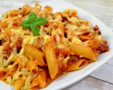 Penne z sosem pomidorowym i kawałkami pikantnego chorizo, zapieczone pod ciągnącym się serem, ozdobione listkiem bazylii.