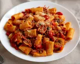 Pyszny makaron z sosem pomidorowym, grzybami i parmezanem na białym talerzu.