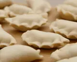 Surowe pierogi z jagodami leżą na drewnianej desce, gotowe do gotowania.