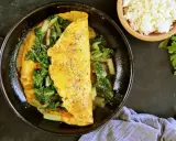 Pyszny omlet na słono z zielonymi warzywami, doprawiony ziołami. Obok miseczka białego sera i natka pietruszki.