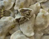 Pyszne pierogi z kapustą i pieczarkami, jeden przekrojony, by pokazać bogate nadzienie. Złoty widelec obok.