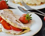 Słodki omlet z bitą śmietaną i truskawkami, posypany cukrem pudrem i płatkami migdałów. Idealny deser na słodko.