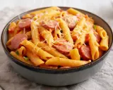 Penne z sosem pomidorowym i plasterkami kiełbasy, posypane startym parmezanem. Pyszne danie makaron z kiełbasą.