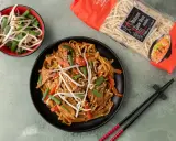 Pyszny makaron chow mein z warzywami i kiełkami fasoli na czarnym talerzu, obok paczka makaronu i miseczka kiełków.