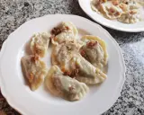 Pyszne pierogi z kapustą i grzybami, posypane skwarkami, na białym talerzu.