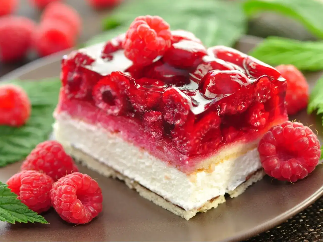 Pyszne ciasto z malinami i mascarpone, oblane galaretką, z malinami i listkami mięty na talerzu.