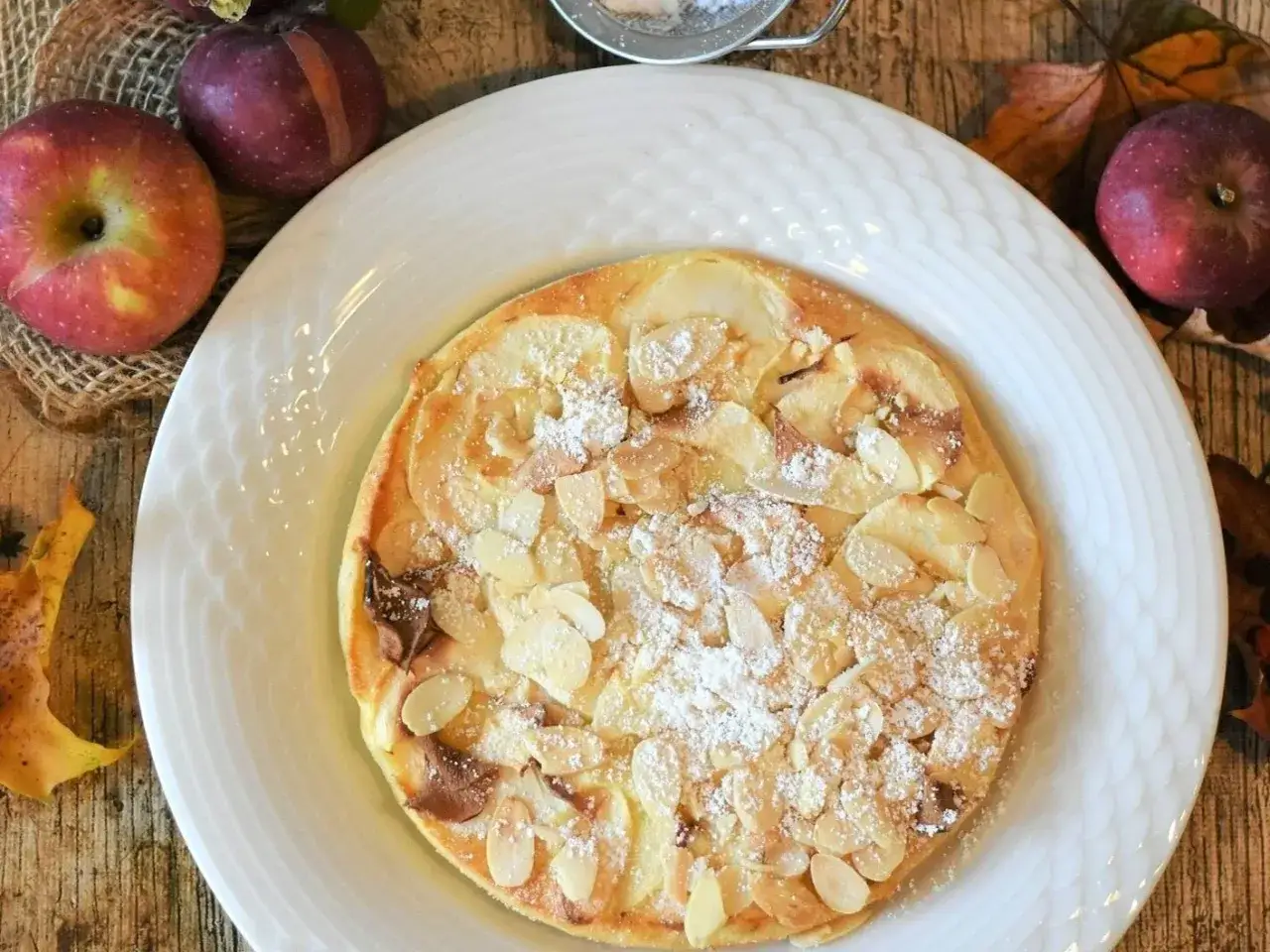 Pyszny omlet z jabłkiem, posypany płatkami migdałów i cukrem pudrem, wygląda apetycznie.