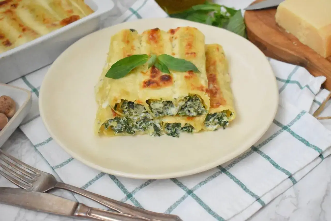 Pyszne cannelloni ze szpinakiem, zapieczone pod beszamelem i serem, ozdobione listkiem bazylii.