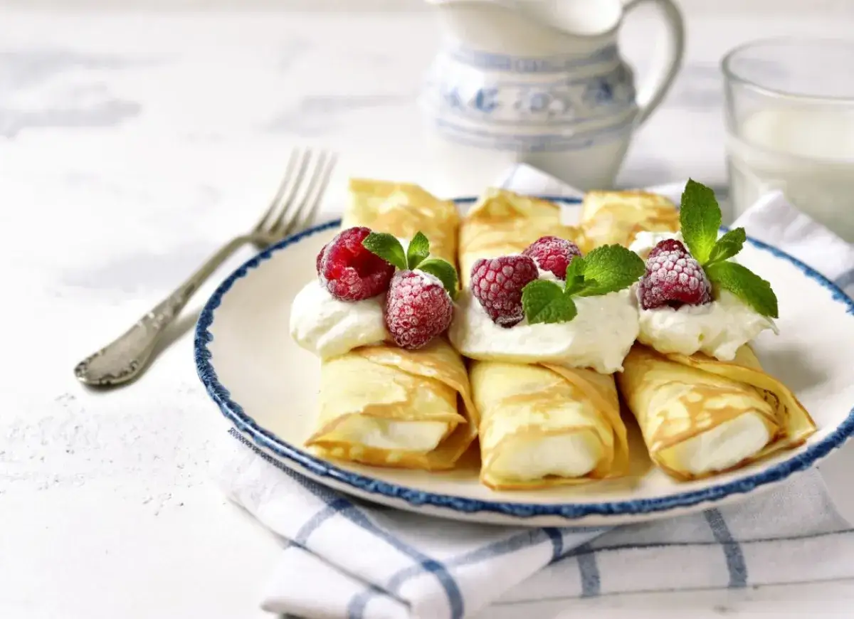 Pyszne naleśniki z mascarpone, udekorowane malinami i miętą, czekają na talerzu.