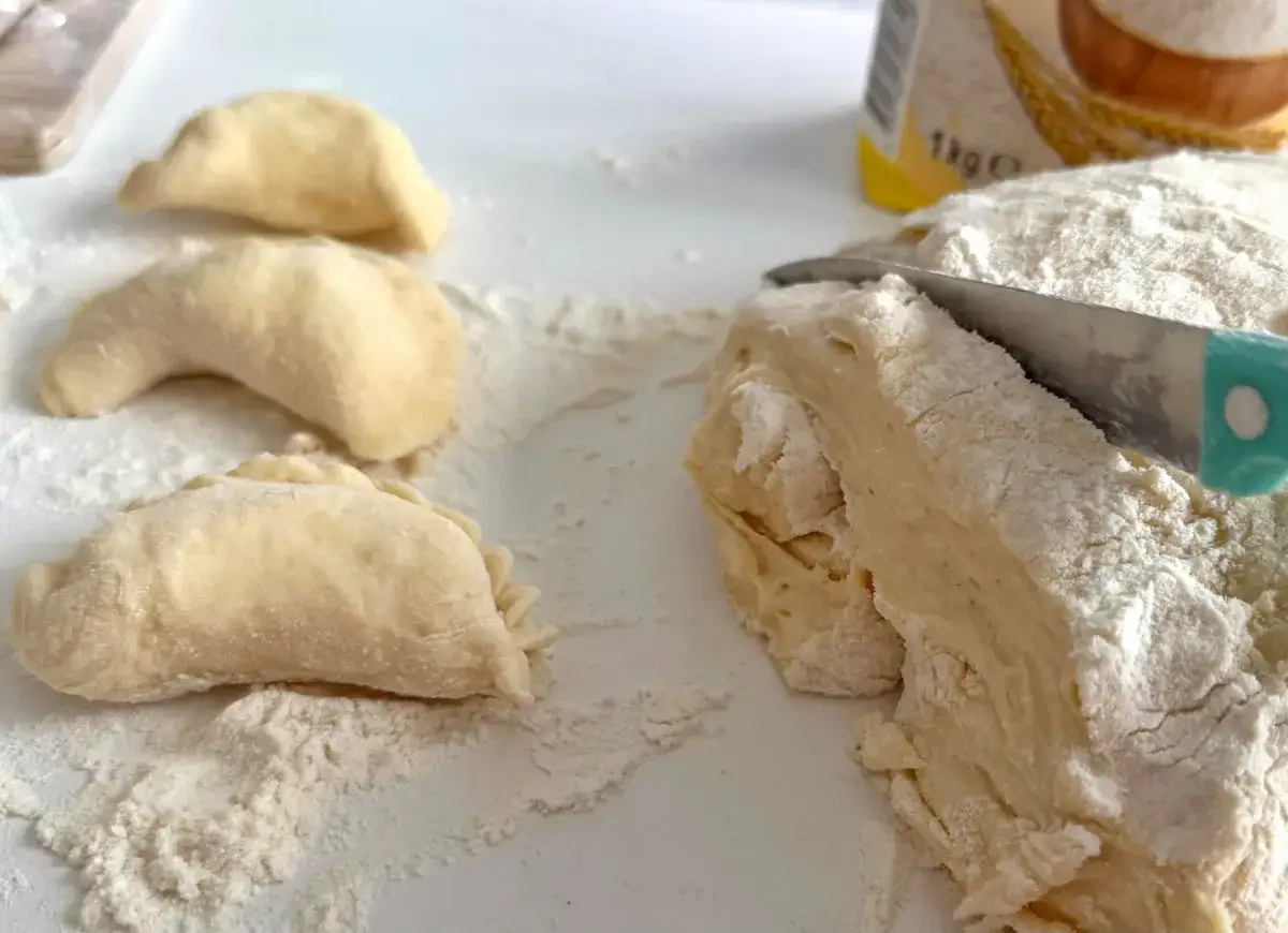 Przygotowuję ciasto na pierogi. Na blacie leżą uformowane pierożki, a obok nóż kroi świeże ciasto.