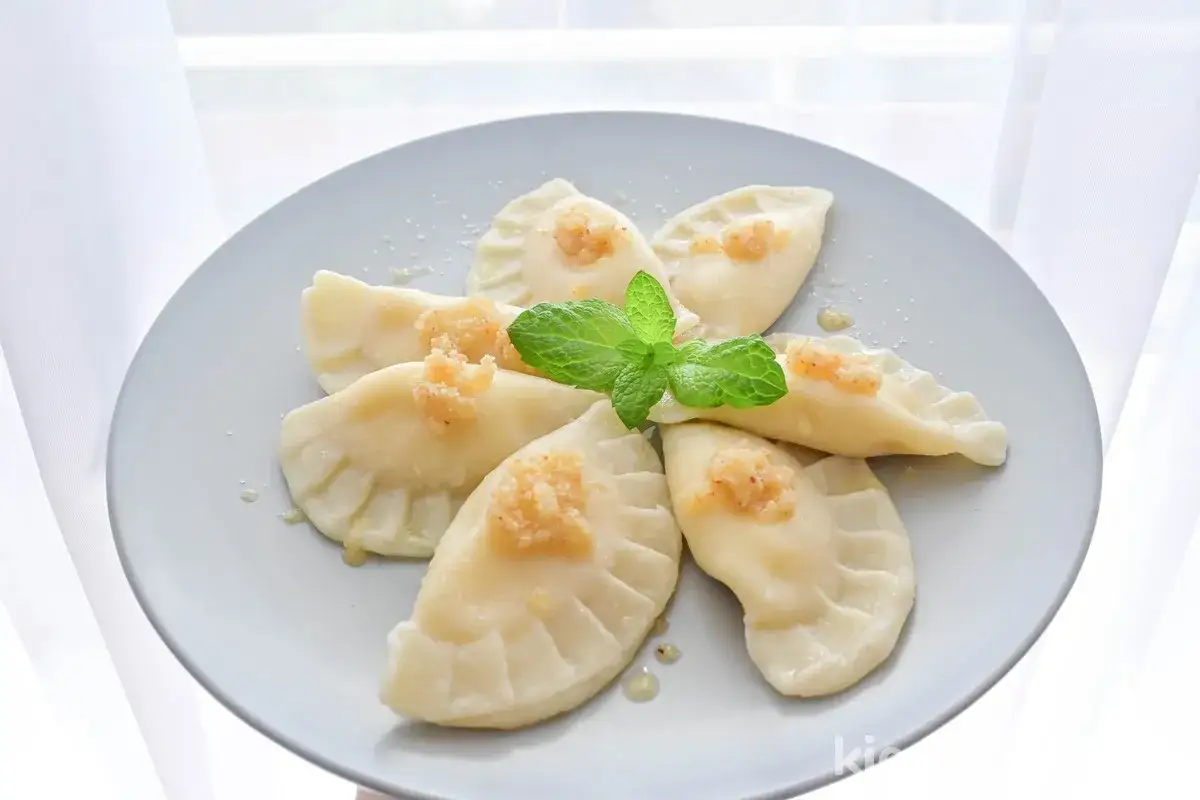 Pyszne pierogi z serem, ułożone na talerzu w kształt kwiatu, ozdobione miętą i okrasą.