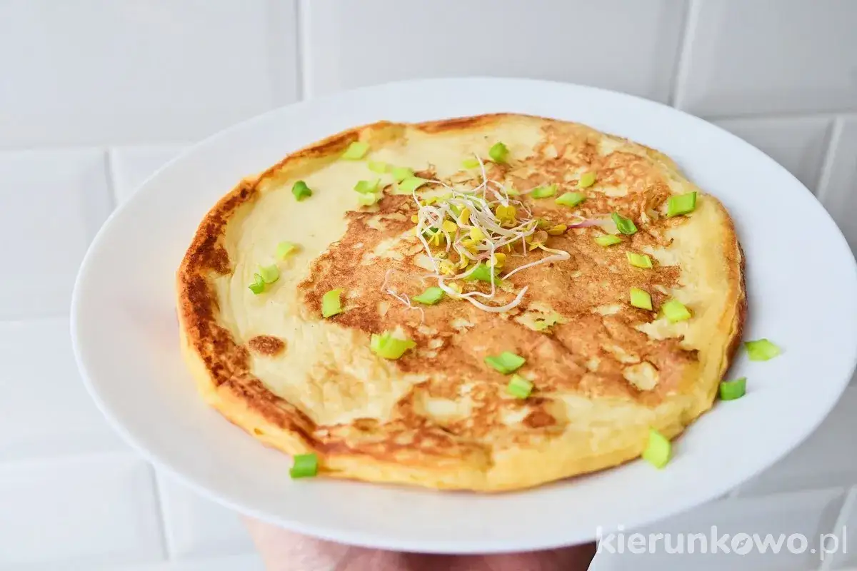 Pyszny omlet na słono, ozdobiony kiełkami i szczypiorkiem, czeka na śniadaniowy apetyt.