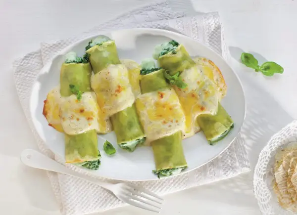 Pyszne cannelloni ze szpinakiem, zapieczone pod kremowym sosem serowym, ozdobione listkami bazylii.